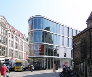 Glasfassade eines Einkaufshauses im Erfurter Stadtzentrum. Retail-Immobilie für den Einzelhandel von unserem Büro für Immobilienbewertung sachlich und unabhängig begutachtet. Glasgebäude zwischen einem Jugendstilgebäude und einer frühgotischen Kirche.